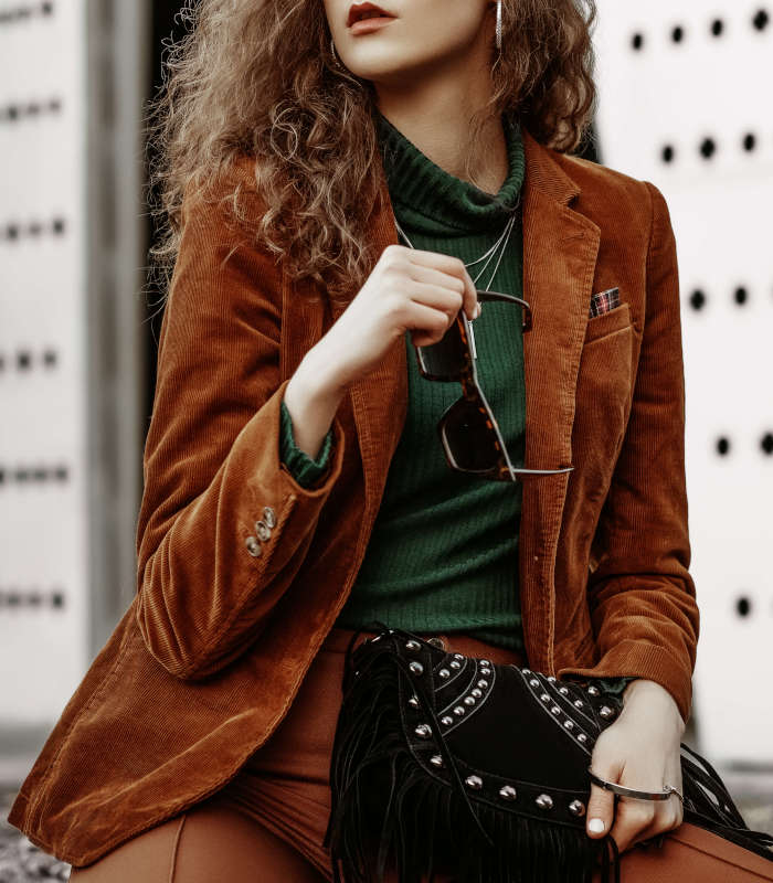Outdoor fashion portrait of young confident fashonable woman wearing brown corduroy blazer, trousers, green turtleneck, necklace, holding black suede bag with fringe, posing in street Chaqueta de seda, lino, terciopelo o de grandes diseñadores Tintorerías Ronsel - Imagen 1